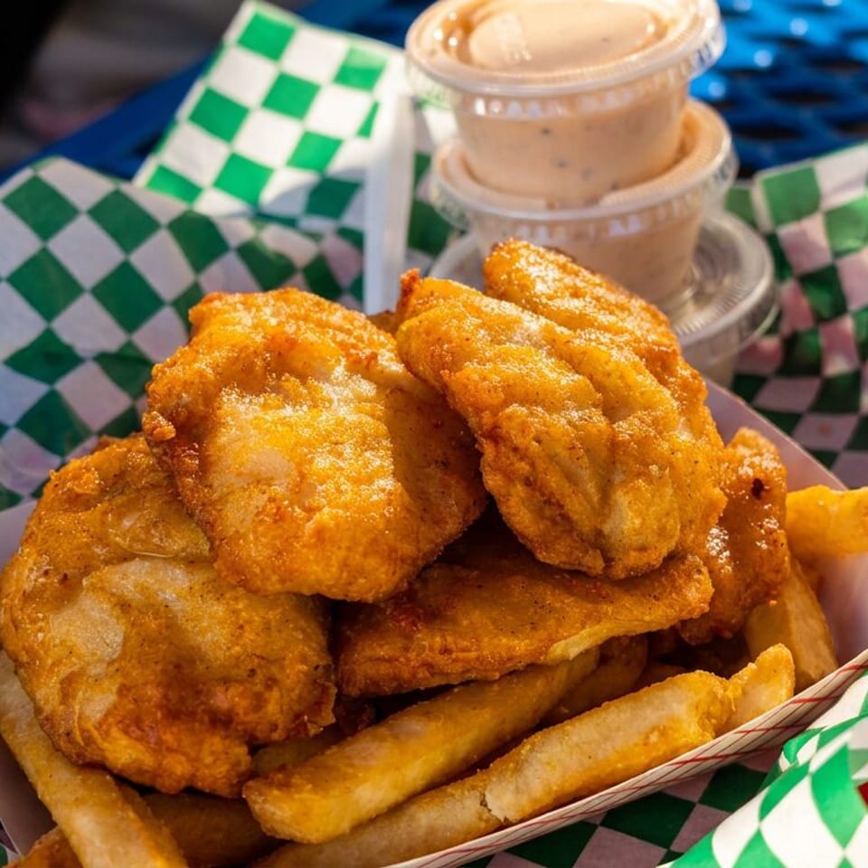 Golden fried fish and chips in a paper tray with green and white checkered lining, with two dipping sauces.